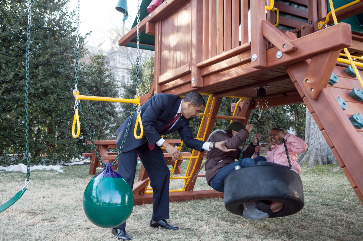 In this official White House photograph, President Barack Obama plays with daughters Malia and Sasha on the new playground swing-set. on the South Lawn of the White House, March 4, 2009.