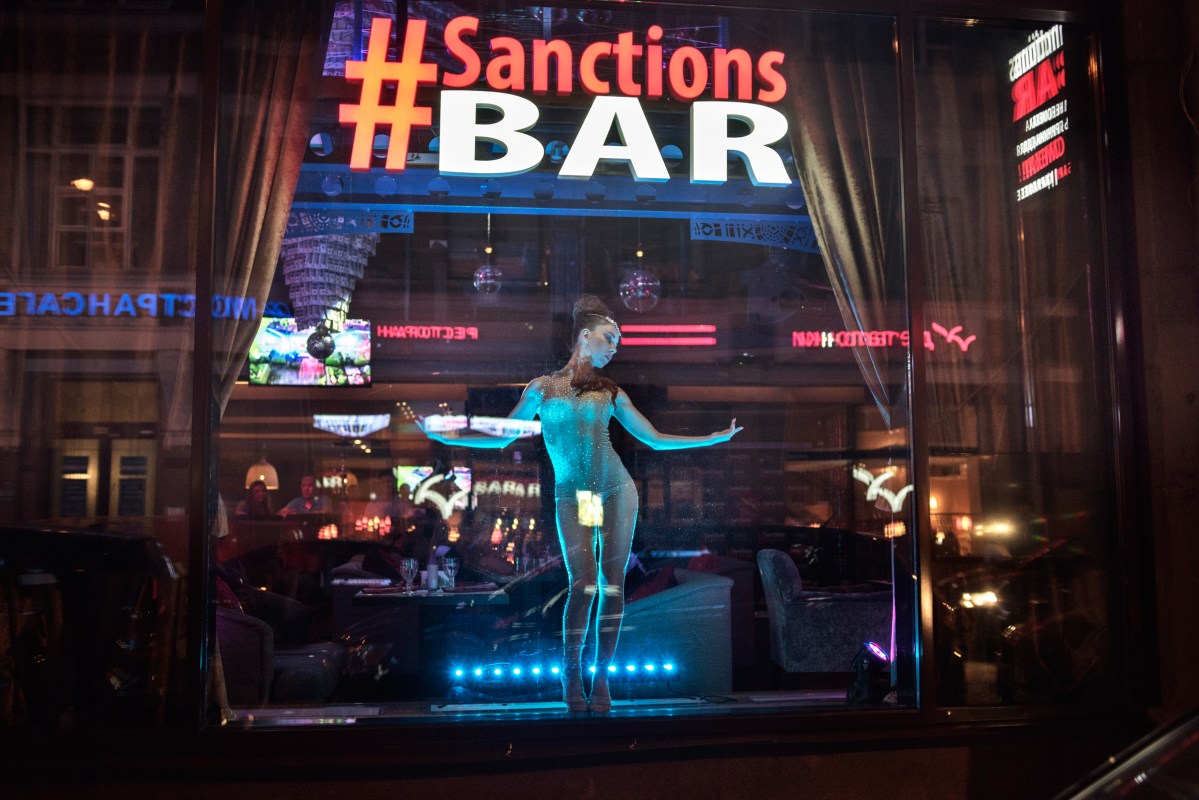 A dancer in the window of the #Sanctions Bar in Moscow, June 2015. Designed to make light of the economic sanctions that the U.S. and its allies imposed on Russia over the conflict in Ukraine, the bar features oil drums, a chandelier draped in fake $100 bills, and a menu poking fun of then-President Barack Obama.