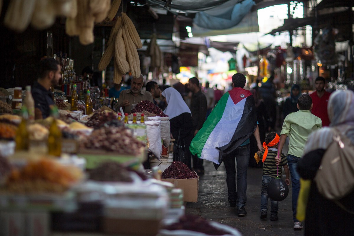 A palestinian man wearing a flag walks through the old central market in Gaza July 14, 2015.