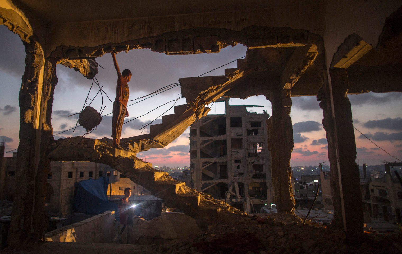 Ten years old Ahmad Al Atawna stands amongst the rubble of his family destroyed house before nightfall during a power outage, in Al Shejaeiya neighbourhood, in the east of Gaza City, 27 July 2015. Residents of Gaza, home to 1.8 Million people, have been experiencing up to 15 to 18 hours of electricity outage a day for the past two weeks due to fuel and power shortages. By Wissam Nassar.