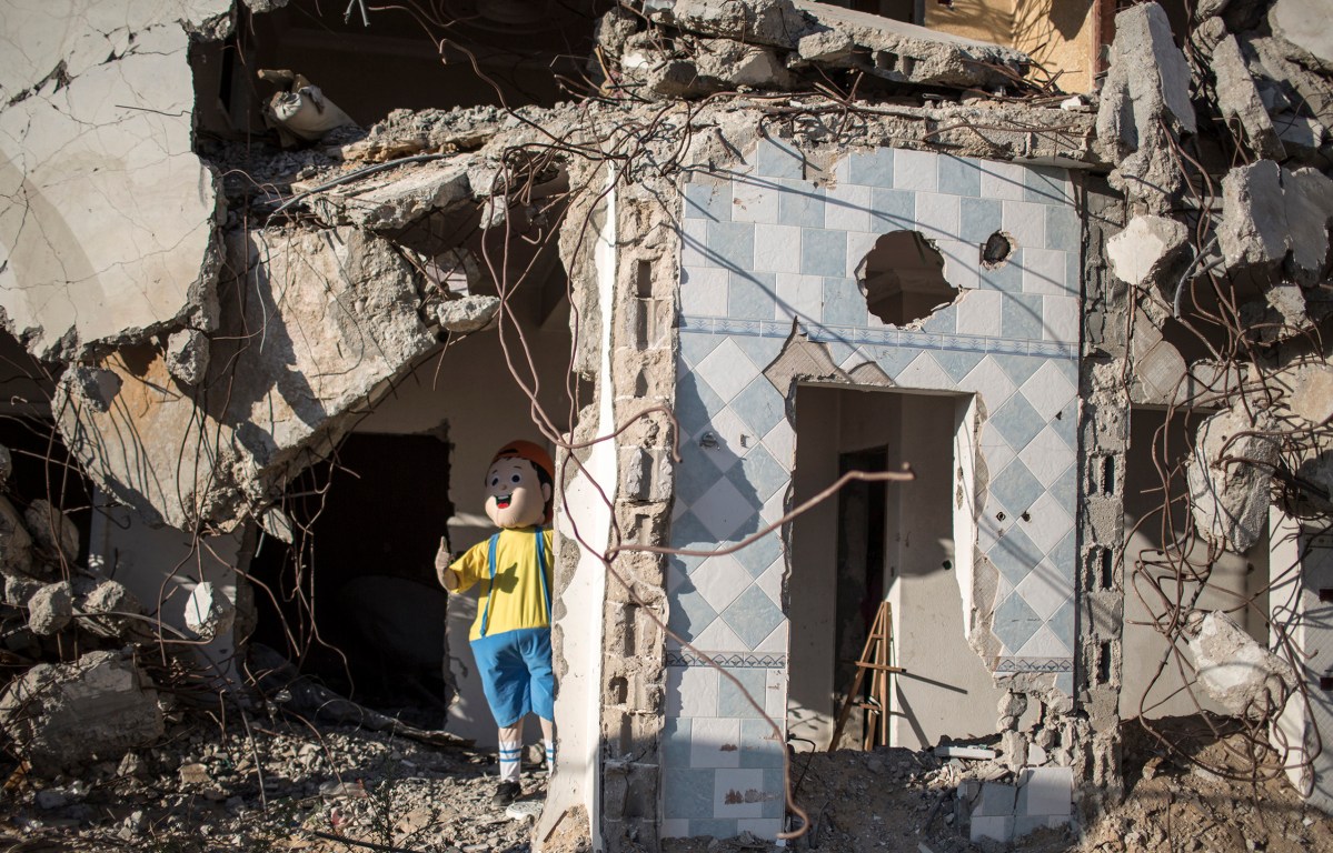 Palestinians dressed in costumes perform during an event for children in front of destroyed houses in Gaza City's Shujaiya neighbourhood on July 8, 2015 on the occasion of the first anniversary of the 50-day war between Israel and Hamas' militants in the summer of 2014.One year ago, a new war erupted between Israel and Palestinians in the Gaza Strip, the third in six years. In the course of the conflict -- the longest, deadliest and most destructive -- 2,251 Palestinians were killed, including 551 children. More than 10,000 were wounded and 100,000 were left homeless. On the Israeli side 73 people were killed, of whom 67 were soldiers. Up to 1,600 were wounded, according to the United Nations. By Wissam Nassar.