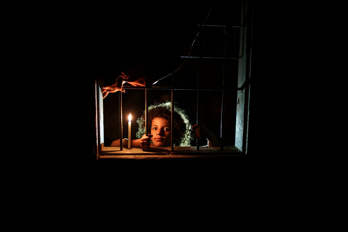 Sara Abushawish, aged 9, is looking through the window of her family courrugated iron sheet house beside candlelight in al-Zaitoun Nieghborhood in eastern Gaza Strip.on Aug. 12, 2017. Most Palestinian in Gaza Strip use batteries, generators or candles to light their homes. Residents of Gaza, home to 1.8 million people, experience some 20 of electricity outage per day. According to reports, the Gaza Strip sole functioning power on 16 April 2017 ran out of fuel and stopped working. The Gaza Power Generating Compan. By Wissam Nassar.