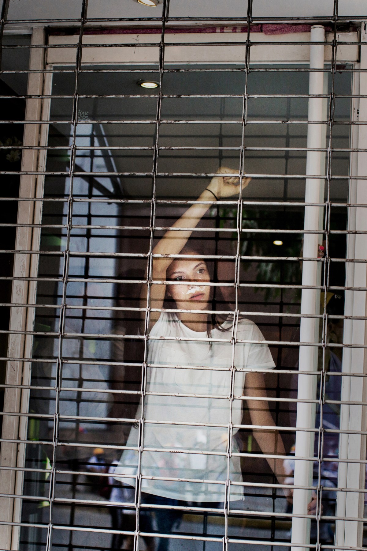 A woman watches from the window of a shuttered store as protesters run from the National Guard in the commercial area of Las Mercedes in Caracas on May 1, 2017.