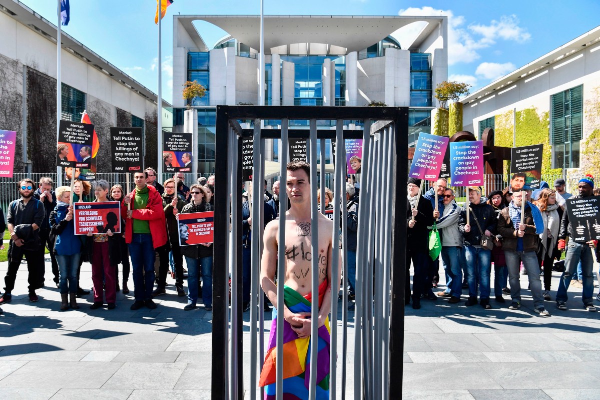 An activist stands naked, wrapped in a rainbow flag, in a mock cage in front of the Chancellery in Berlin on April 30, 2017, during a demonstration calling on Russian President to put an end to the persecution of gay men in Chechnya