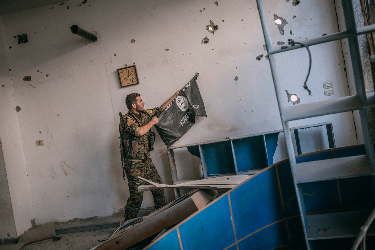 A member of the Syrian Democratic Forces removes an Islamic State flag from a wall in Raqqa on Oct. 18, 2017.